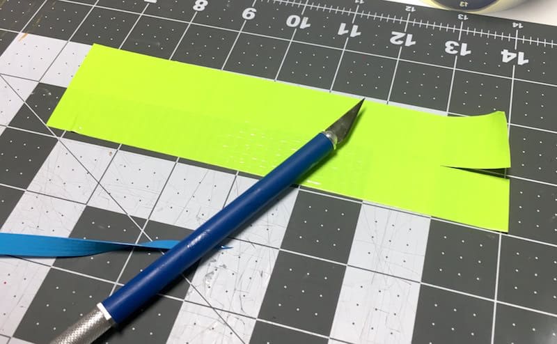 Cutting a 1" slit into neon yellow Duck Tape with a craft knife