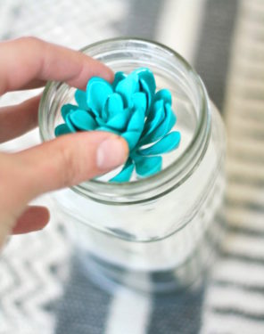 Placing a faux succulent into a mason jar with sand