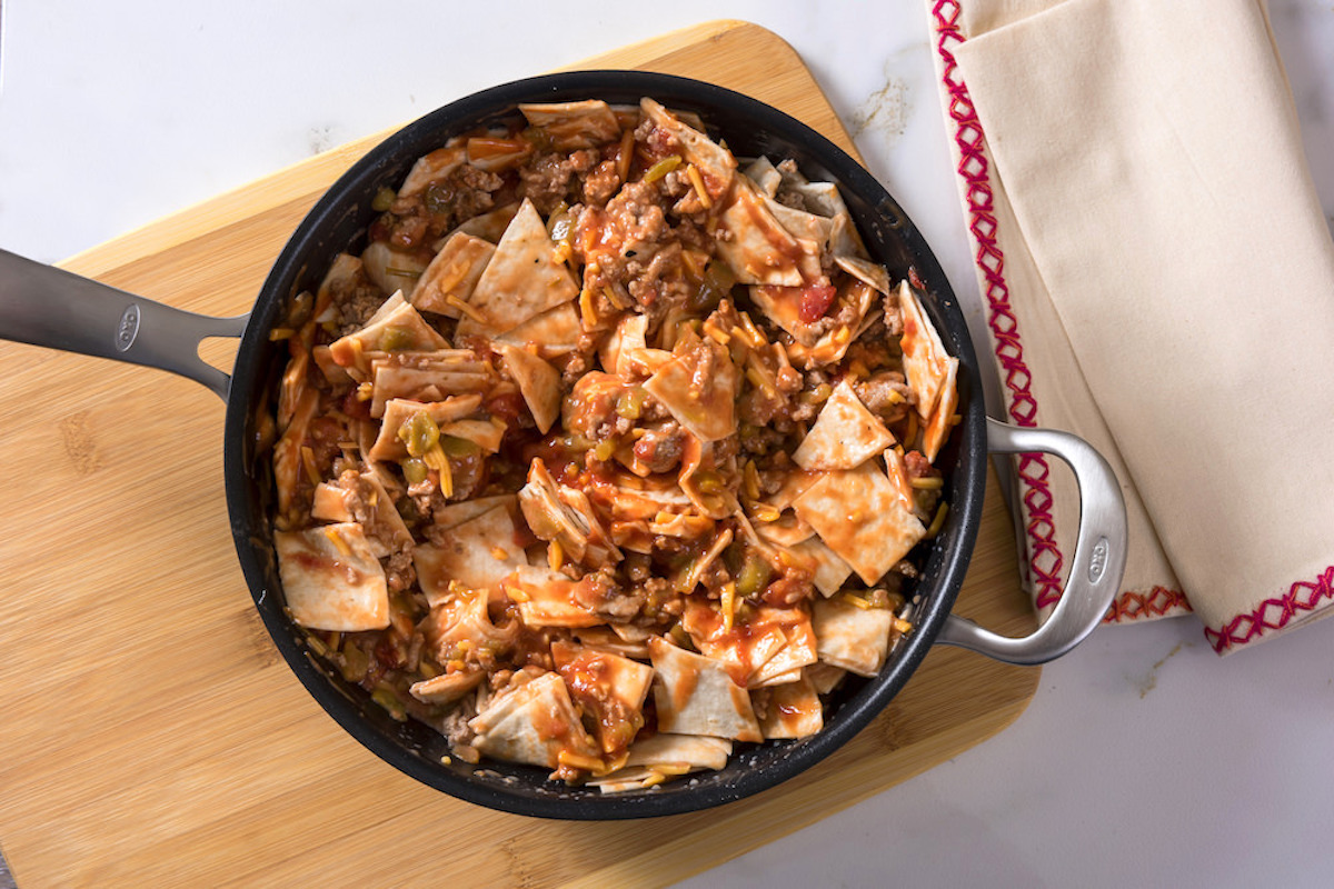 Tortilla pieces, salsa, milk, cheese, and chilis added to a skillet with ground turkey