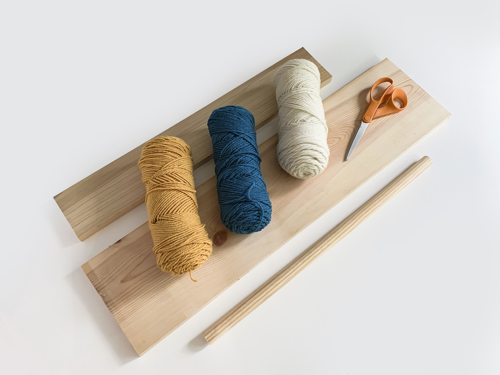 Three skeins of yarn with a dowel rod wood board and scissors