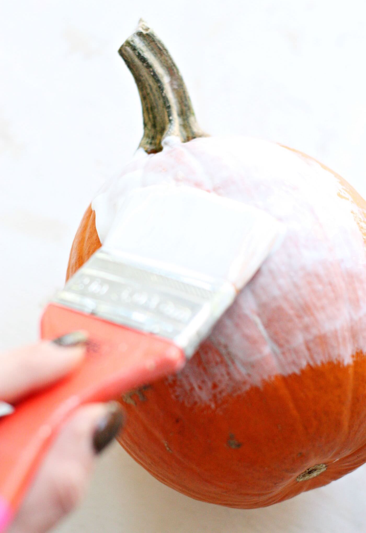Painting a layer of Mod Podge on a pumpkin