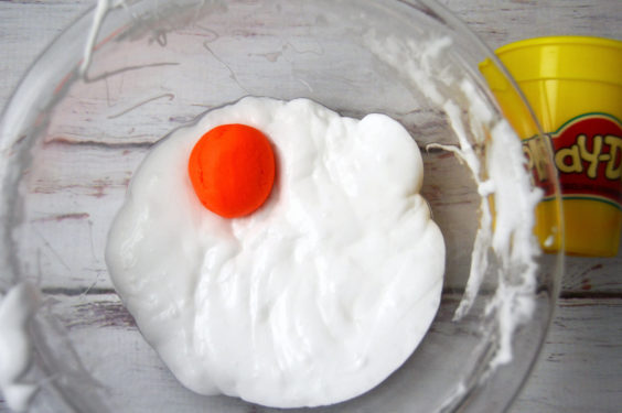 Adding play doh into the slime mixture in a glass bowl