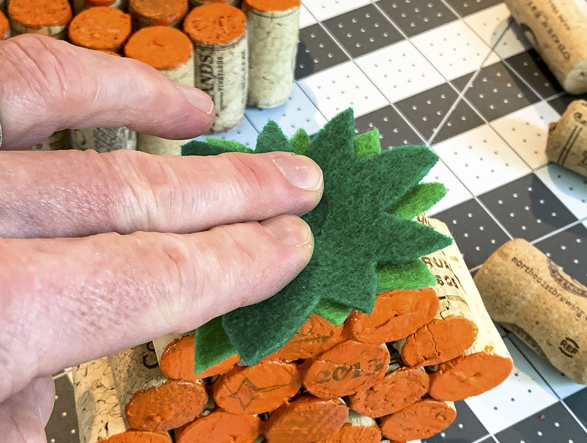 Hot gluing green felt stems to the top of a wine cork pumpkin