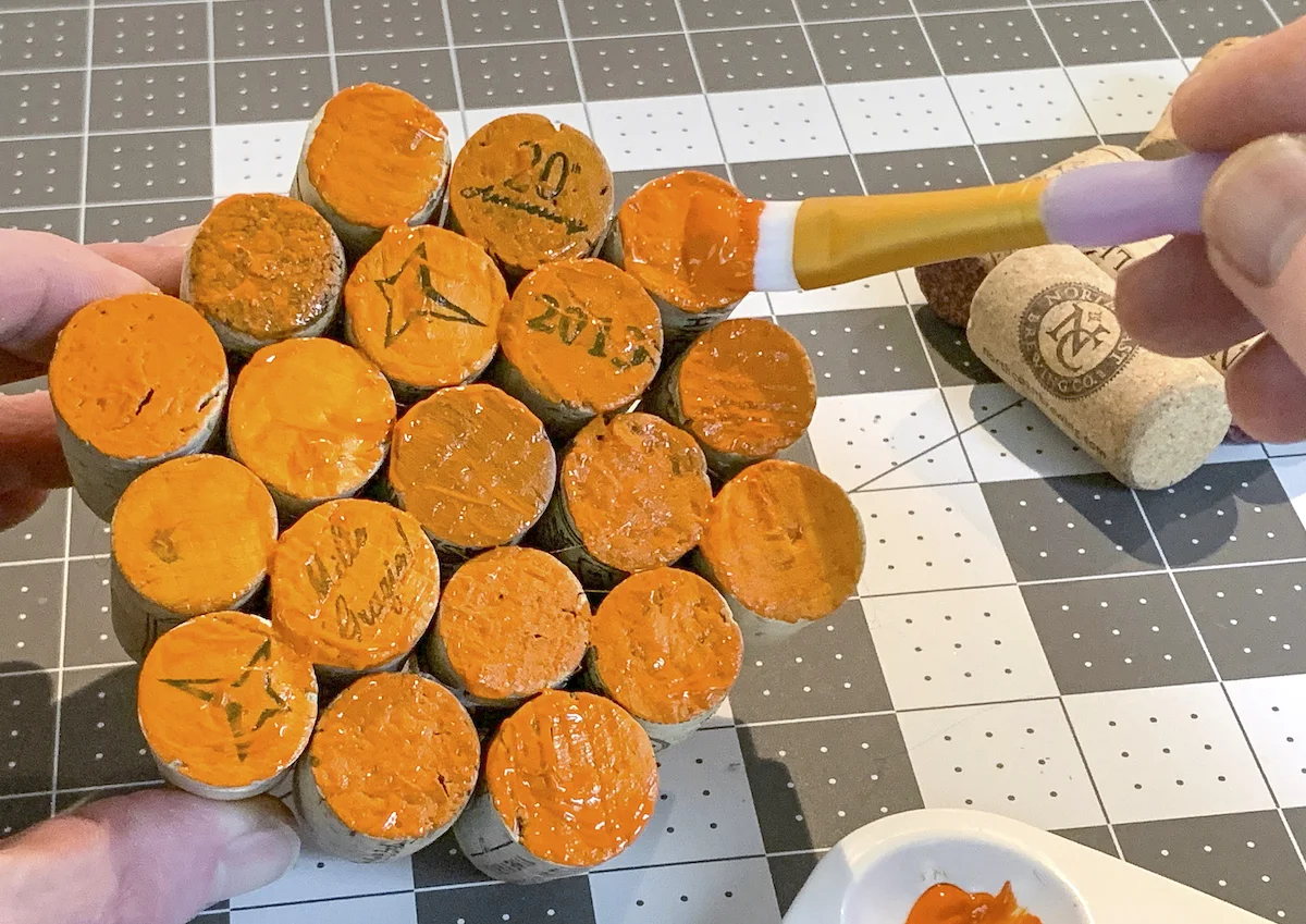 Painting the ends of wine corks with orange acrylic paint and a paintbrush