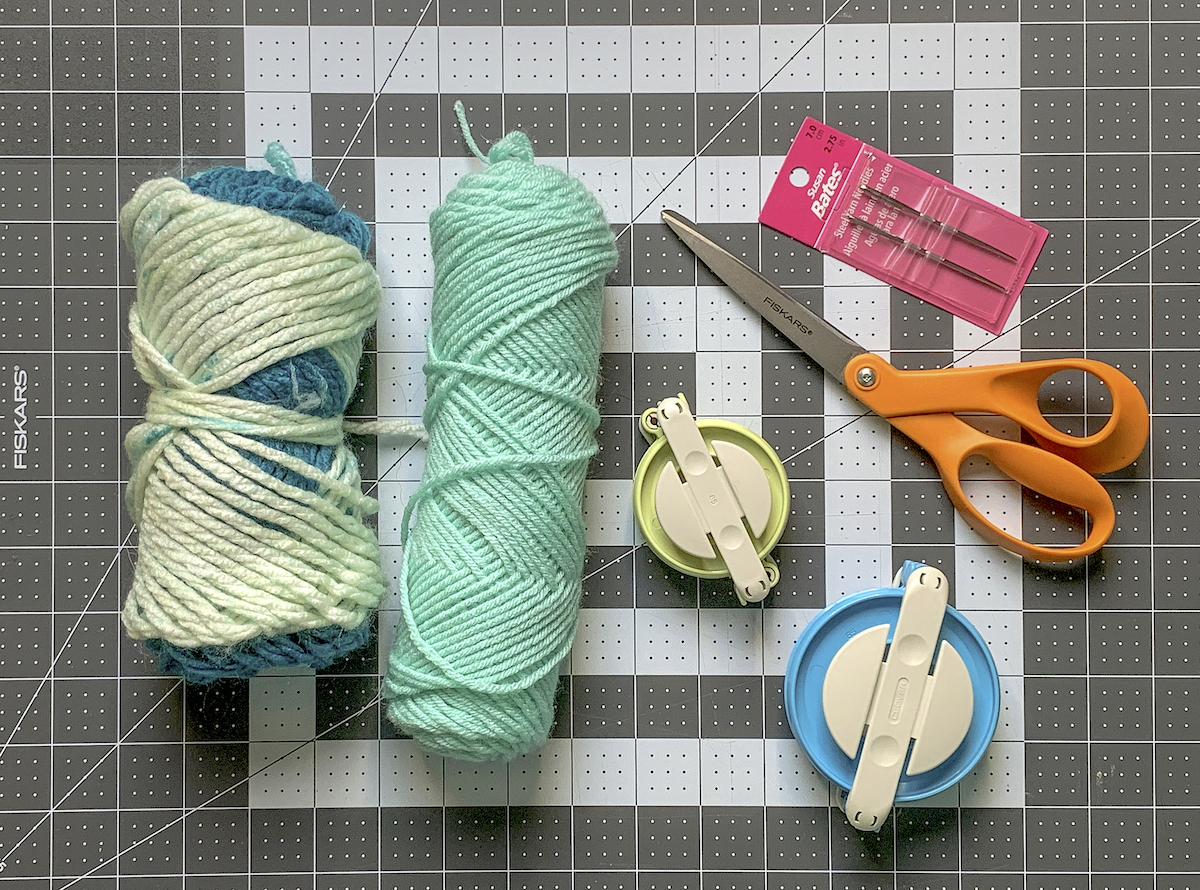 Two skeins of yarn with pom pom makers scissors and needles