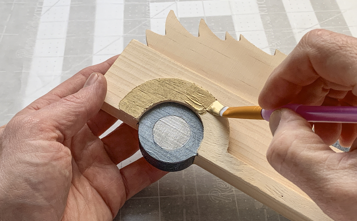 Painting the wheel well of a wood truck shape with gold paint
