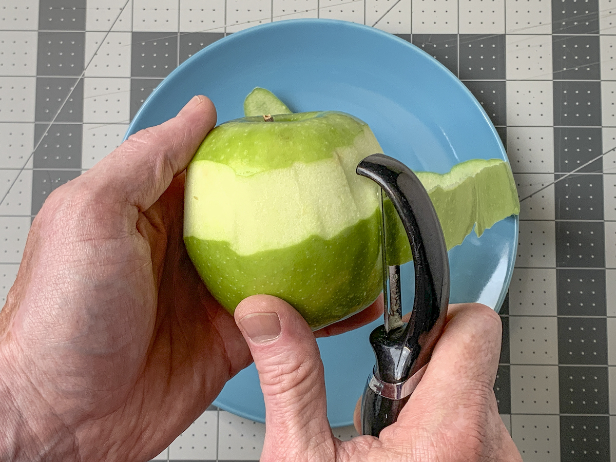 Peeling a green apple with a peeler