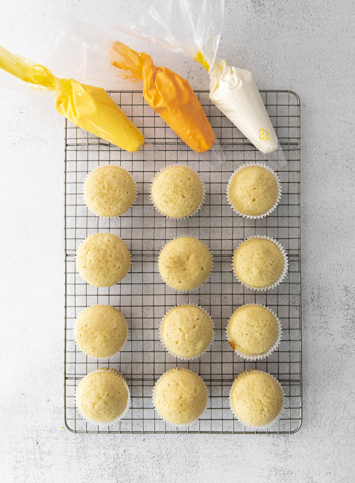 Plain vanilla cupcakes with orange, yellow, and white icing bags