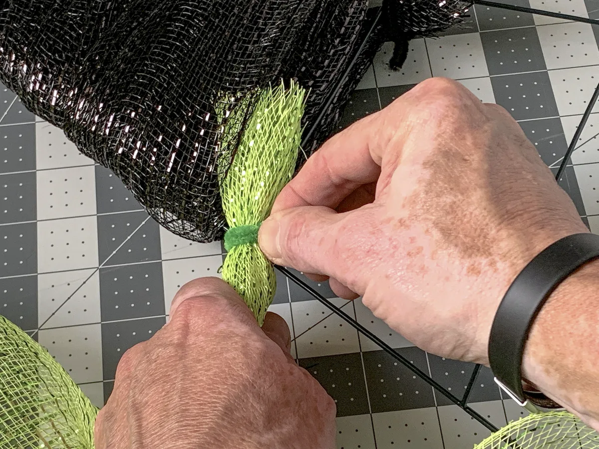 Securing green deco mesh to the middle of the wreath form with a pipe cleaner