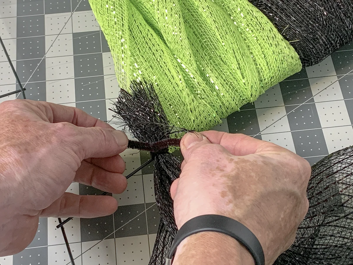 Securing the black mesh down to the wreath form using a pipe cleaner