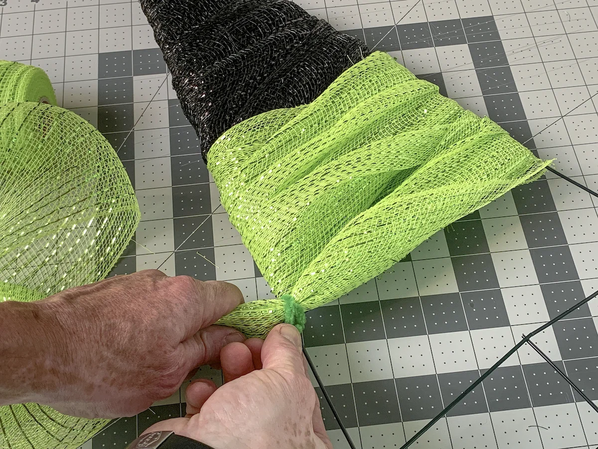 Securing the green deco mesh to the wreath form with a pipe cleaner