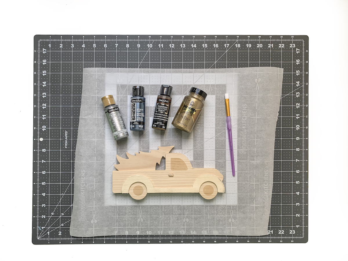 Wood truck shape laying on a surface with acrylic paint bottles