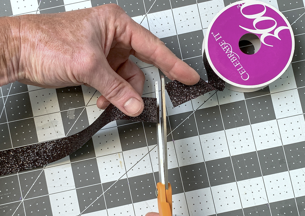 Cutting a piece of black glitter ribbon with scissors
