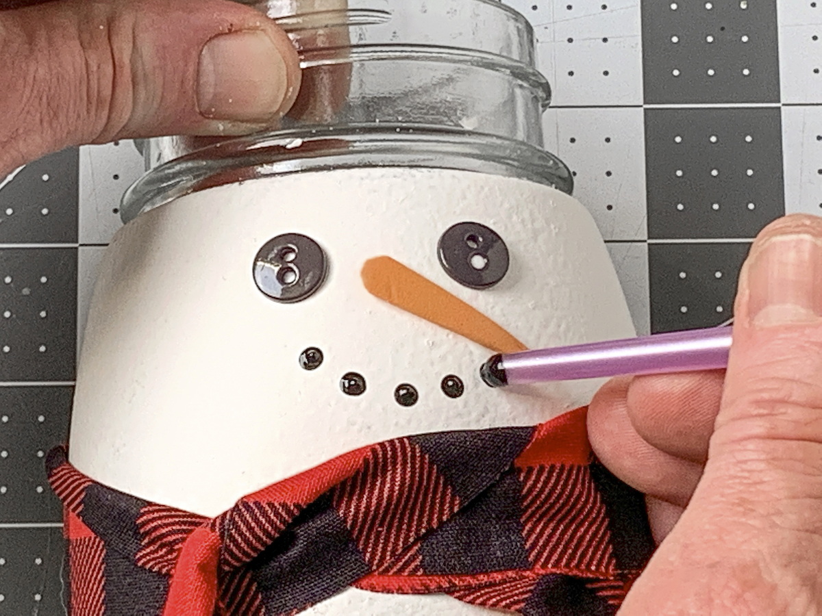 Dotting the snowman's mouth on with the end of a paintbrush and black paint