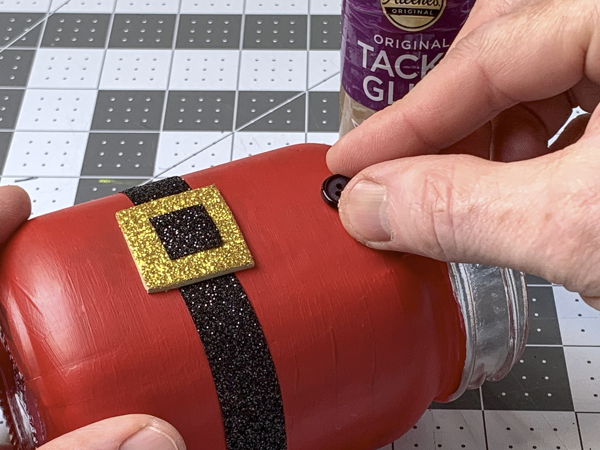 Gluing Santa's black buttons on the front of the mason jar
