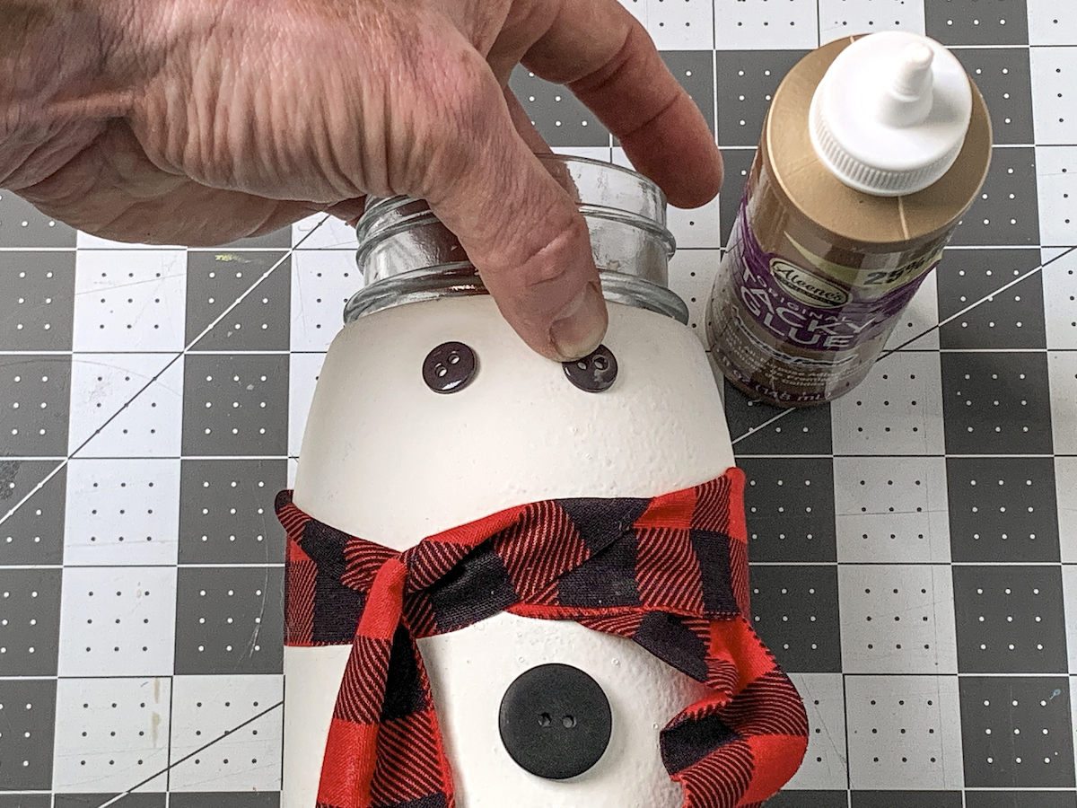 Gluing a button down onto the snowman mason jar for an eye