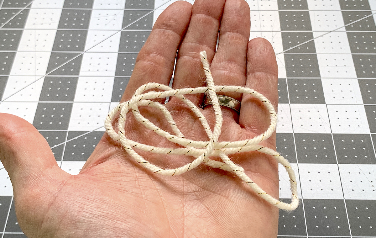 Hand holding a piece of white and gold yarn