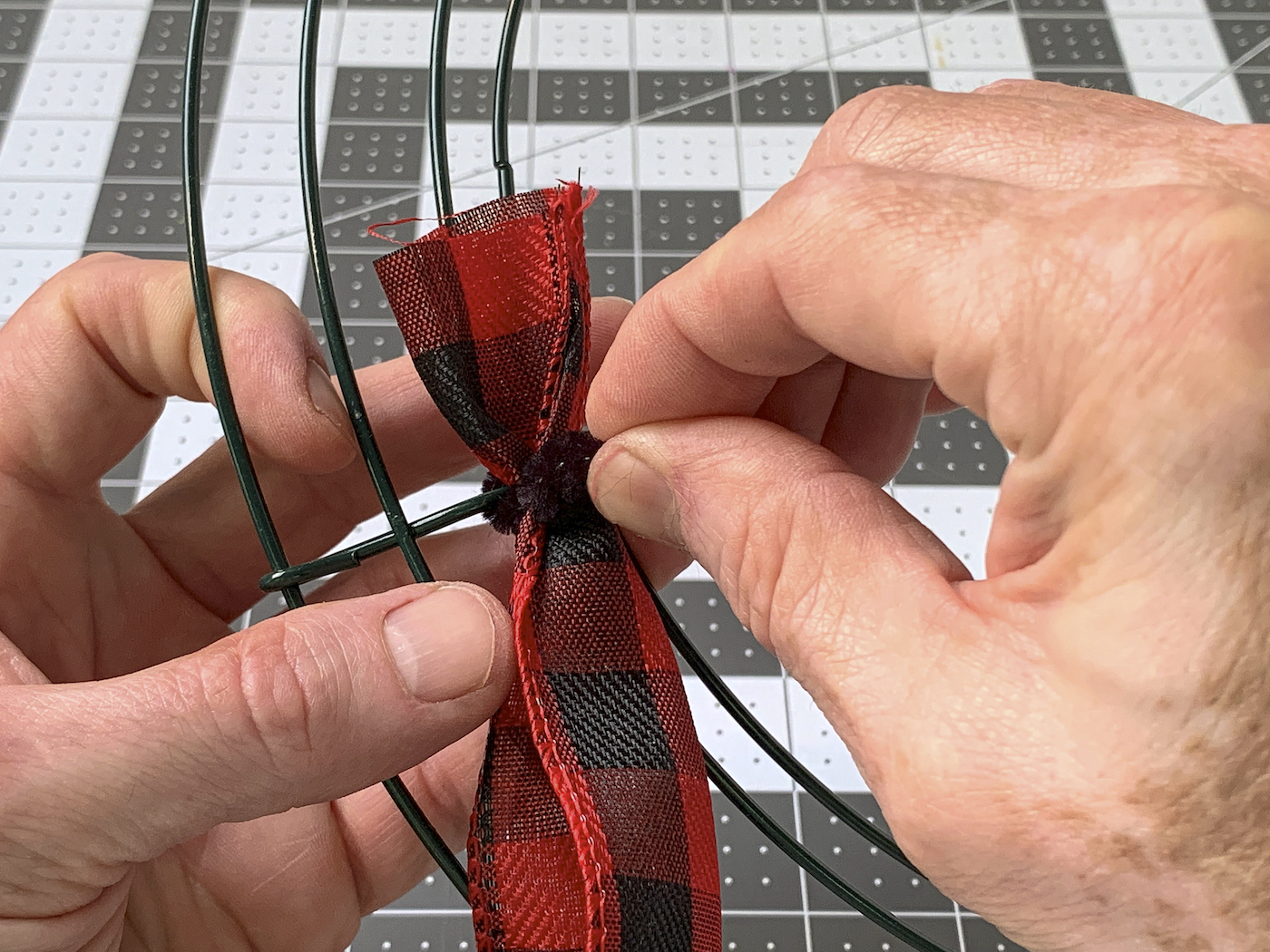 Attaching the end of wire ribbon to the wreath form with a pipe cleaner