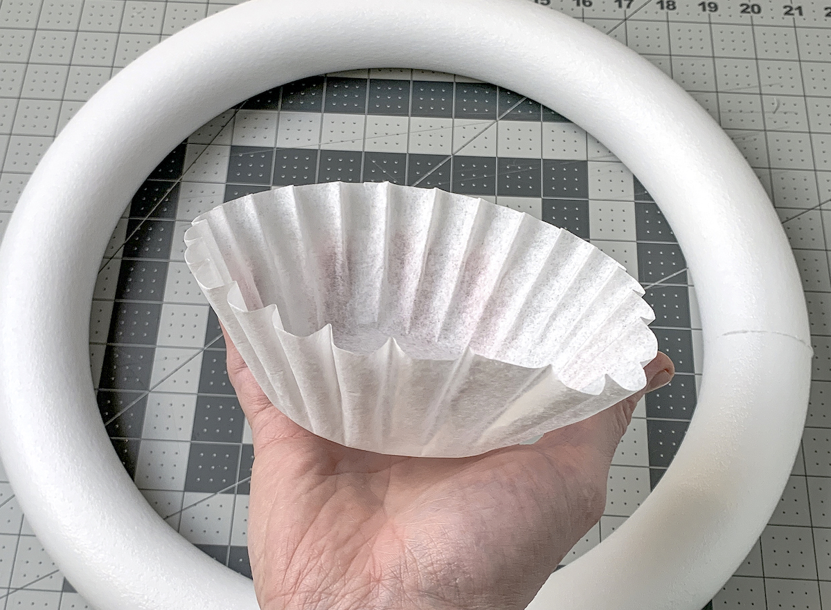 Hand holding a coffee filter in front of a wreath form