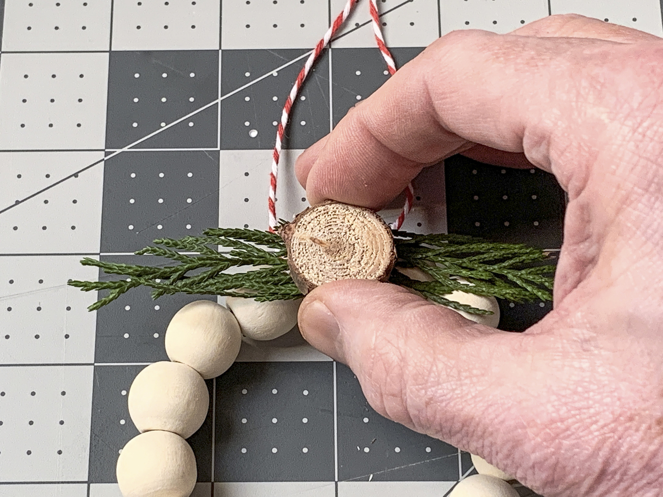 Hot gluing wood circles and fir onto the wooden bead ornament