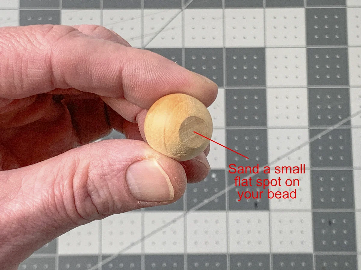 Hand holding a wood bead with one side sanded