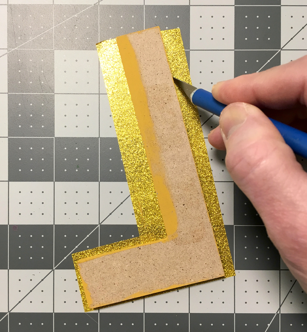 Trimming Gold Duck Tape from around a wood letter with a craft knife