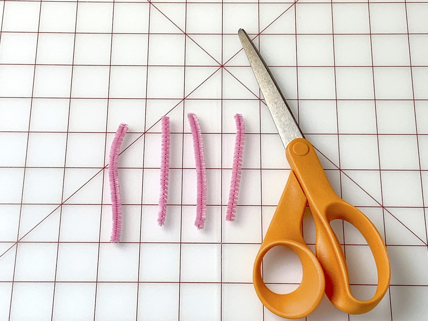 Scissors next to a pink pipe cleaner cut into four pieces