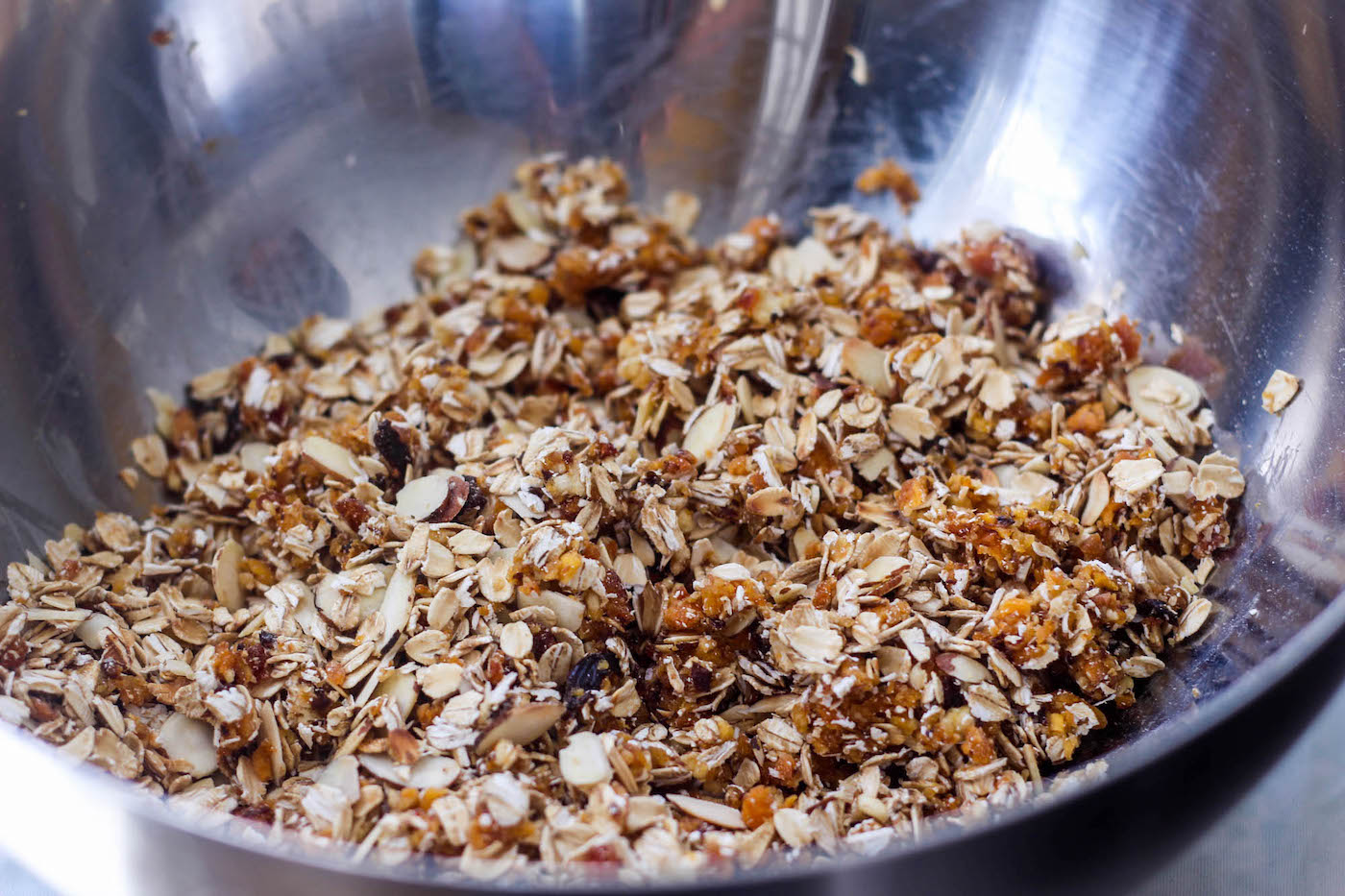 Mixing oats, fruit, and nuts together to make energy bars in a metal bowl