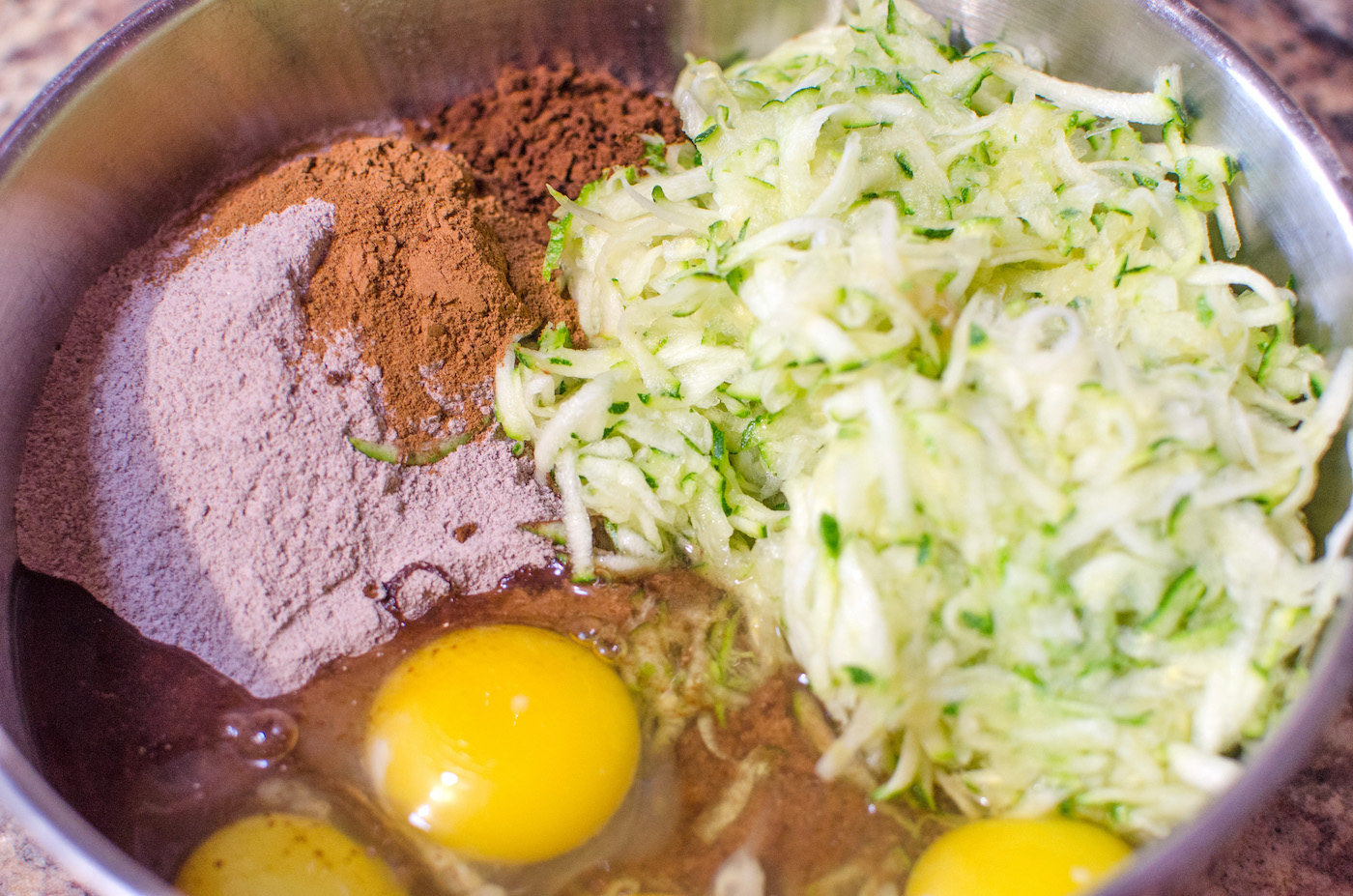 Cake mix, pudding, zucchini, and eggs in a metal bowl