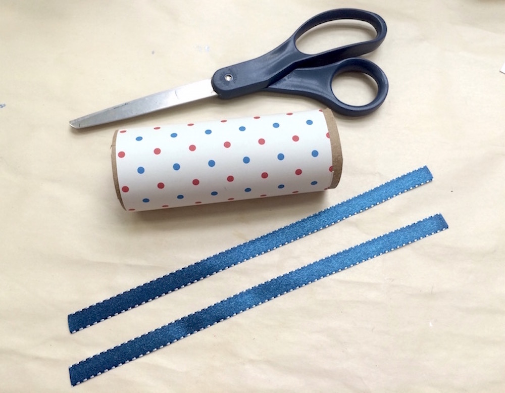 Pair of scissors with a toilet paper tube and two pieces of ribbon