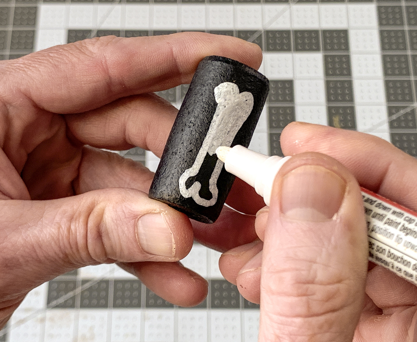 Drawing a bone shape on a black wine cork with a white paint pen