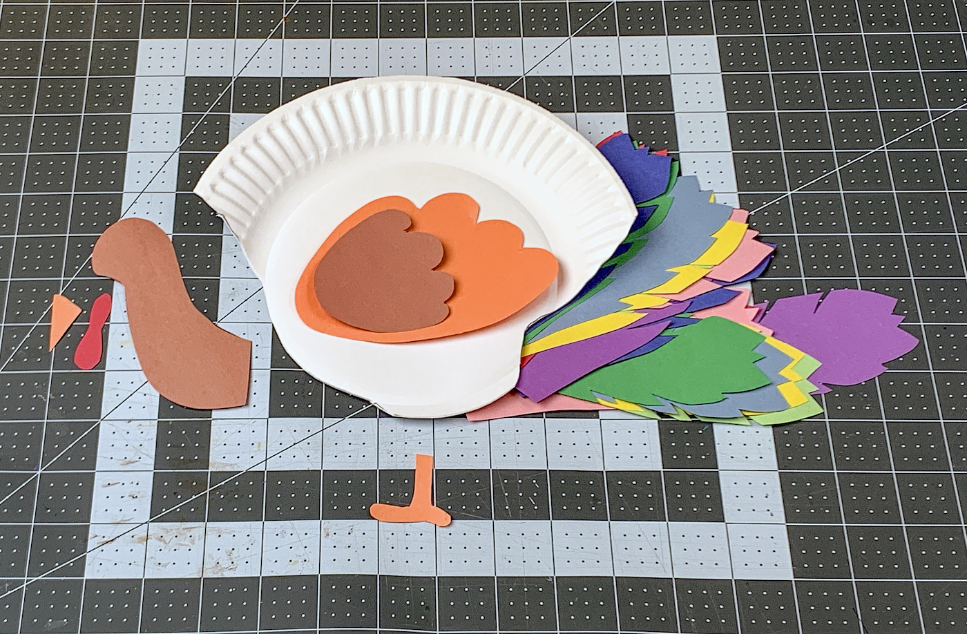 Feathers, paper plate, and turkey parts cut out of paper and assembled on the mat
