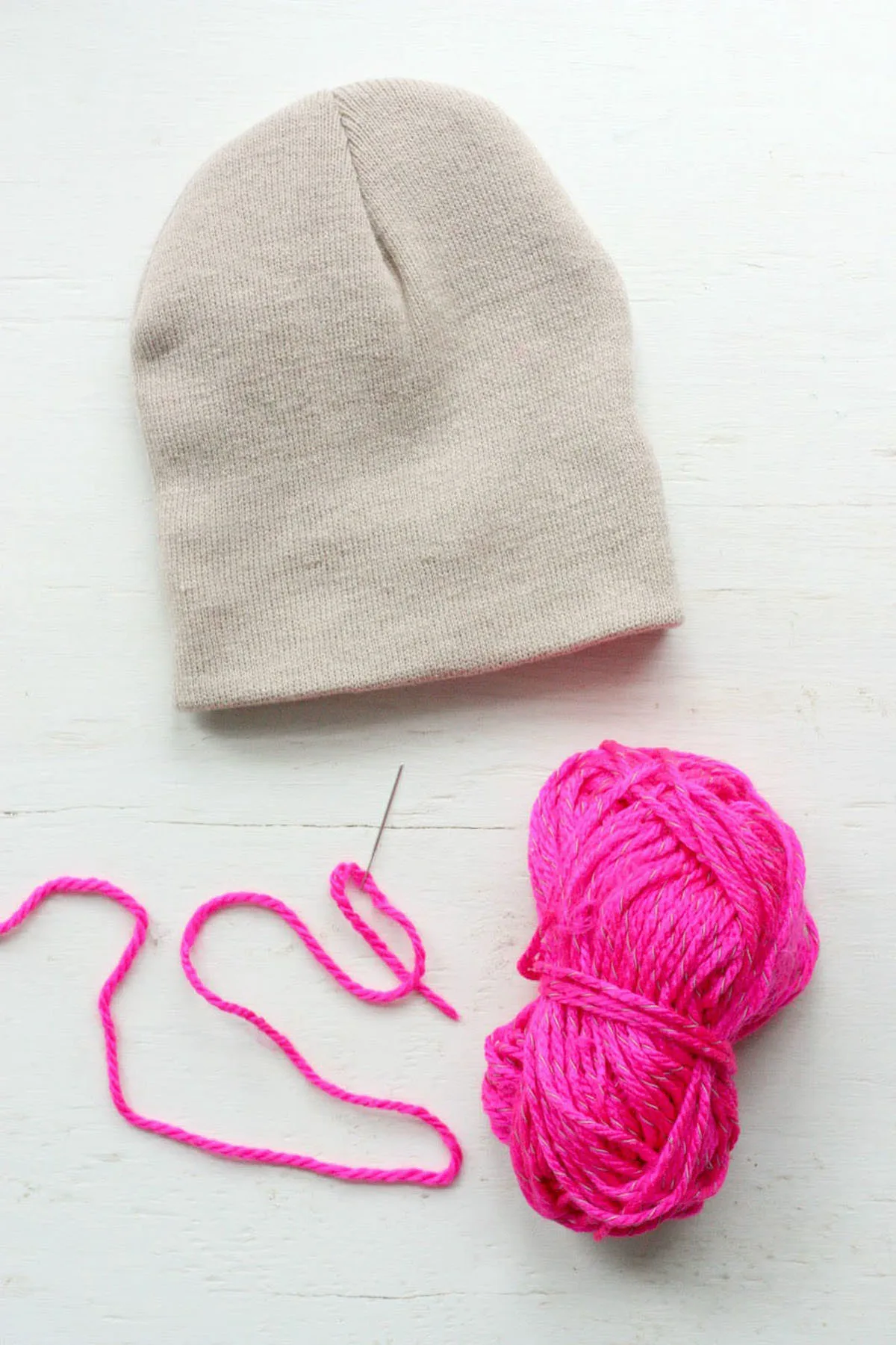 Plain tan beanie with pink yarn on a needle