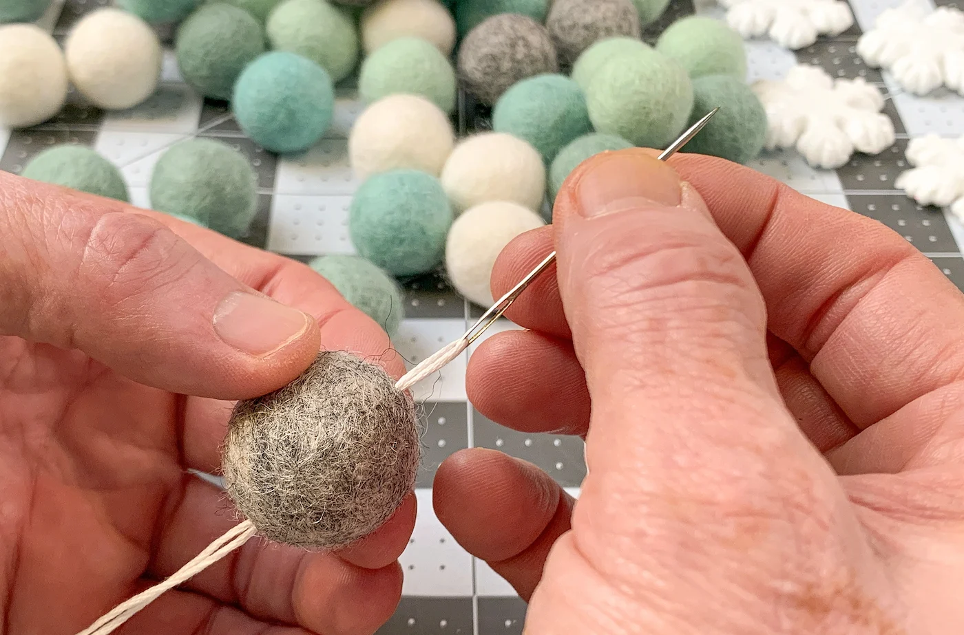 Pulling thread through a gray felt ball