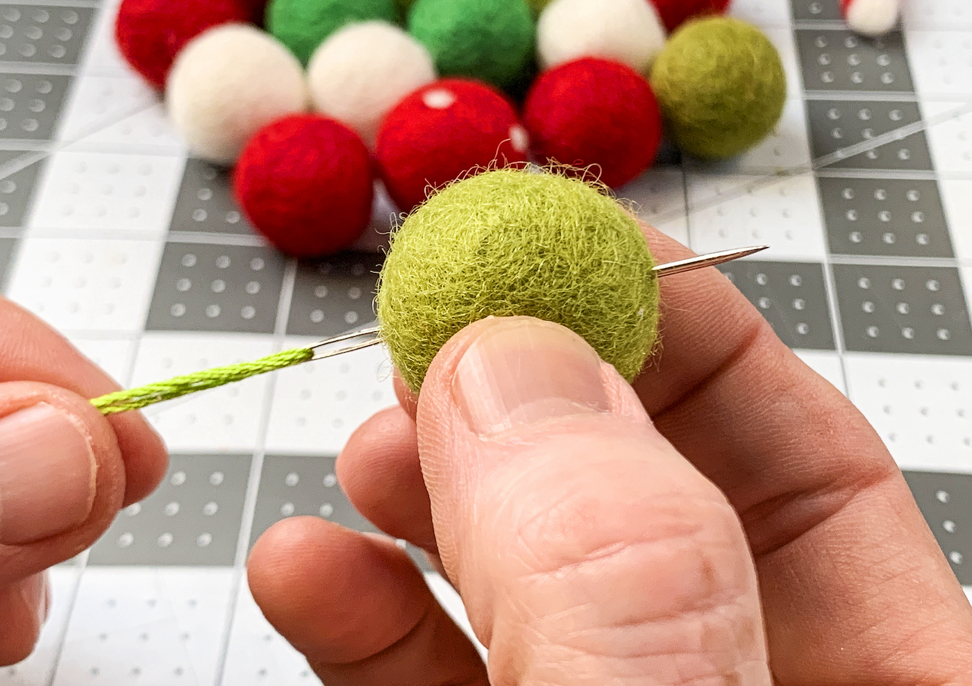 Pushing a needle through a green felt ball