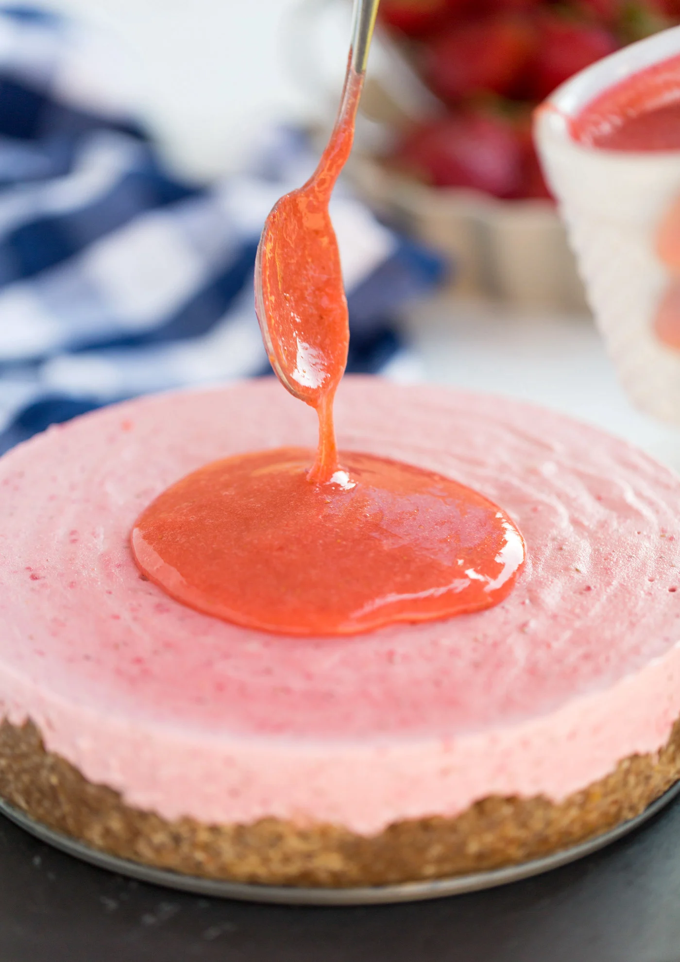 Strawberry glaze being poured onto the strawberry vegan cheesecake