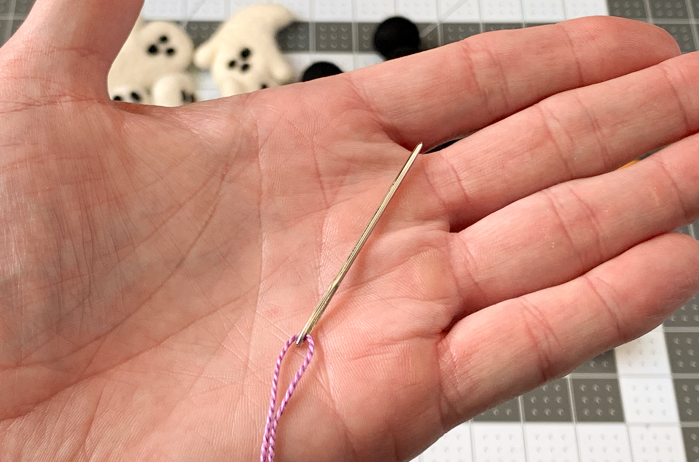Hand holding a needle flossed with purple thread