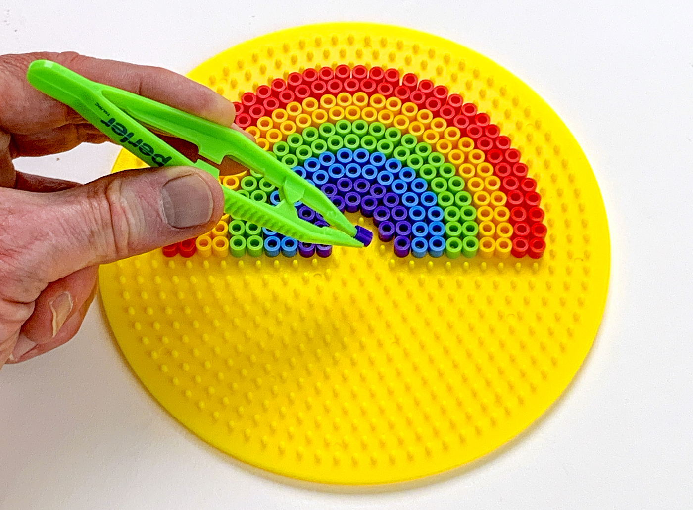 Placing the last purple bead into a rainbow design with tweezers