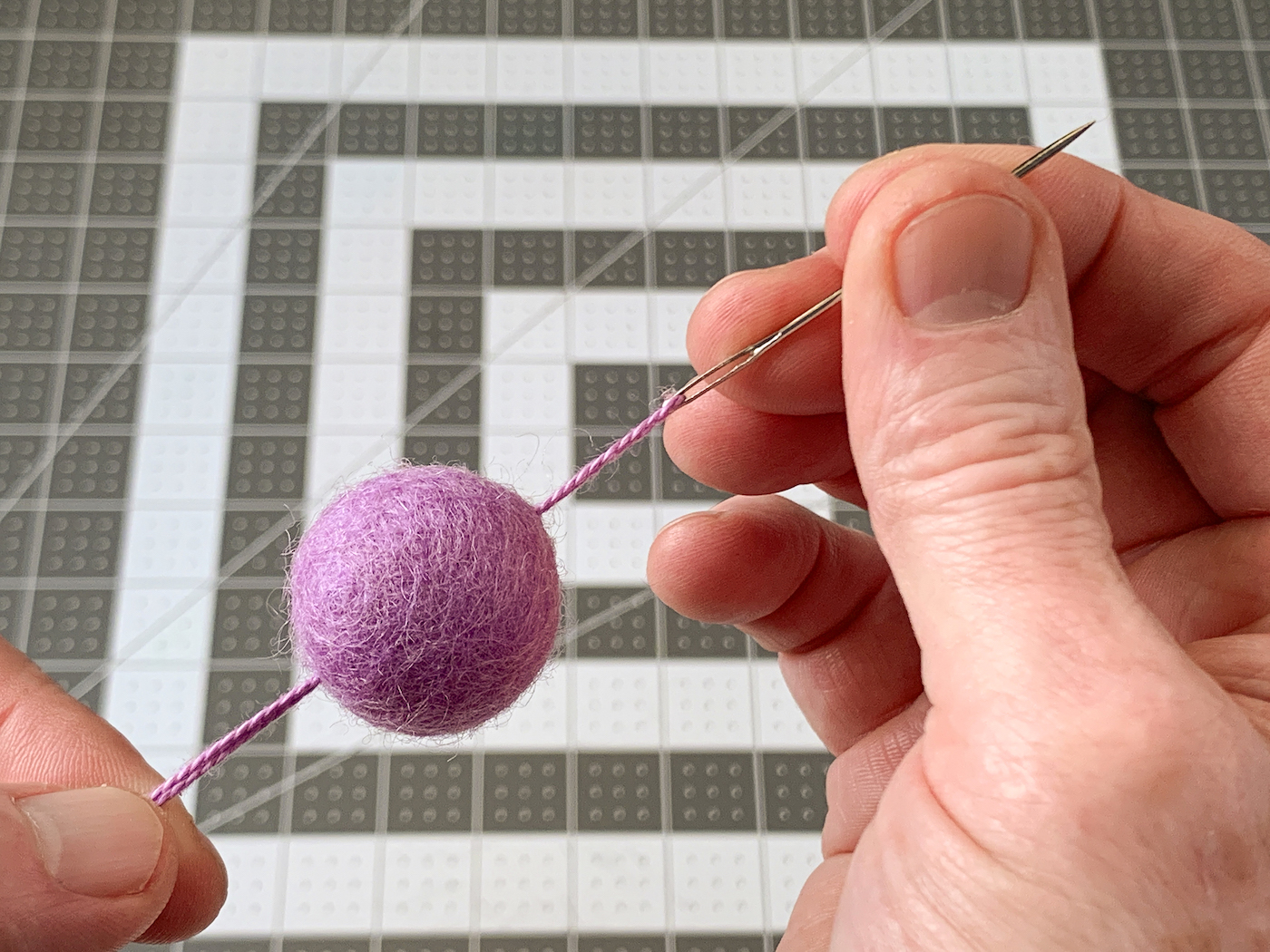 Pulling a needle with floss on it through a purple felt ball