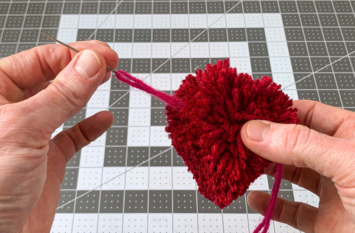 Pulling yarn through the heart pom pom