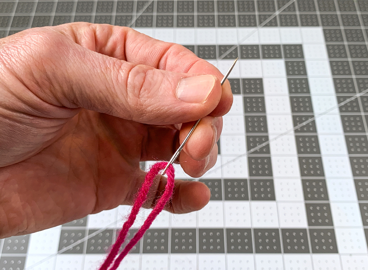 Stringing red yarn onto a tapestry needle