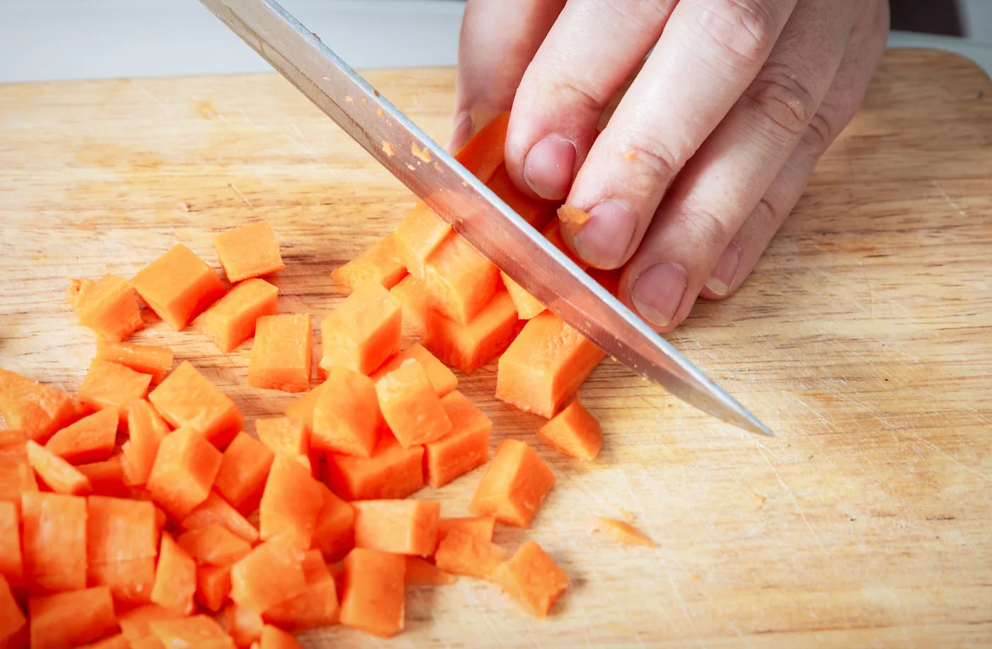 Woman hands chopping carrot on wooden board