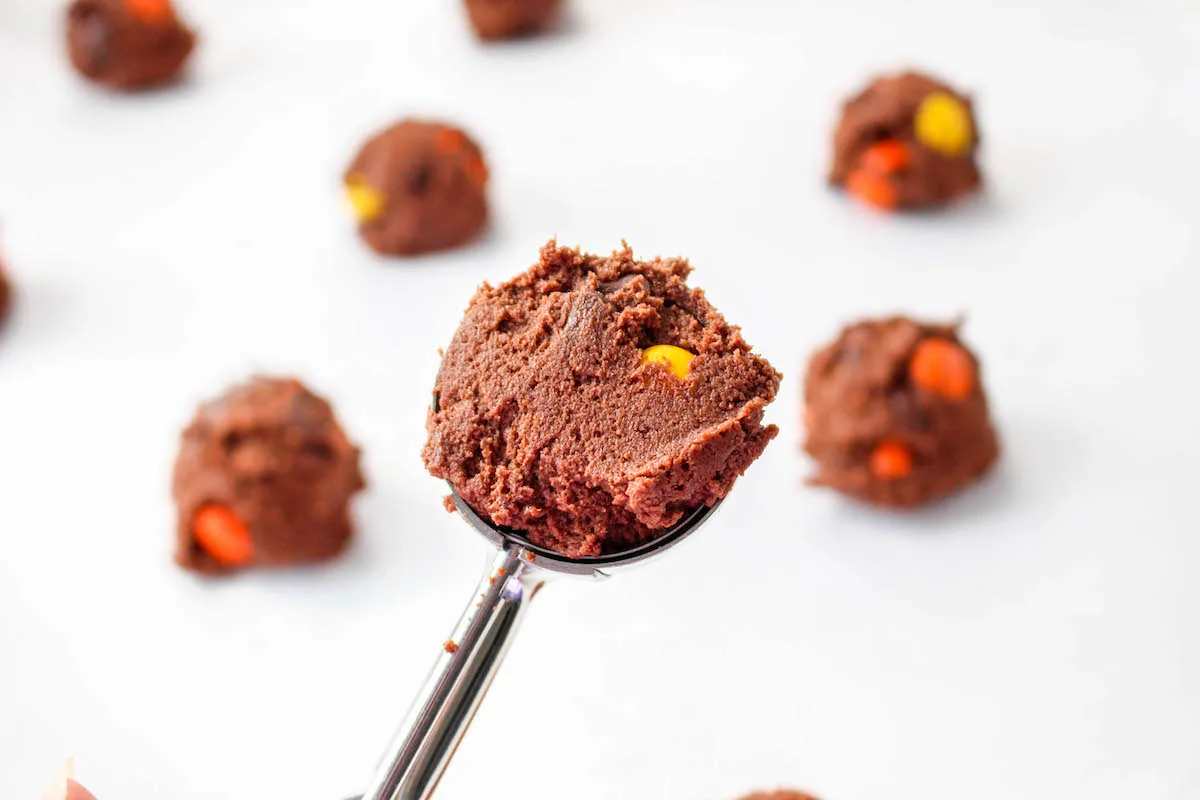 Scooping Reese's pieces chocolate cookie dough onto a baking sheet