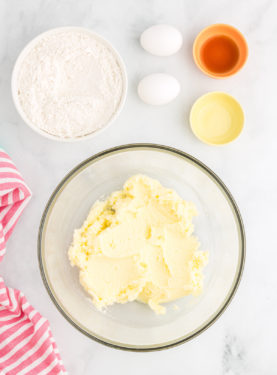 Sugar and butter creamed together in a glass bowl with flour and eggs sitting next to the bowl