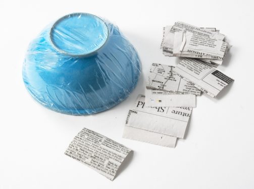 Bowl wrapped in plastic wrap with pieces of newspaper